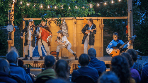 The Three Inch fools performing on a small stage surrounded by people and festoon lights